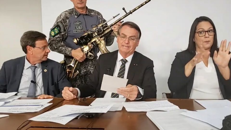 Jair Bolsonaro em live com réplica de fuzil atrás dele. Créditos: Reprodução/Youtube