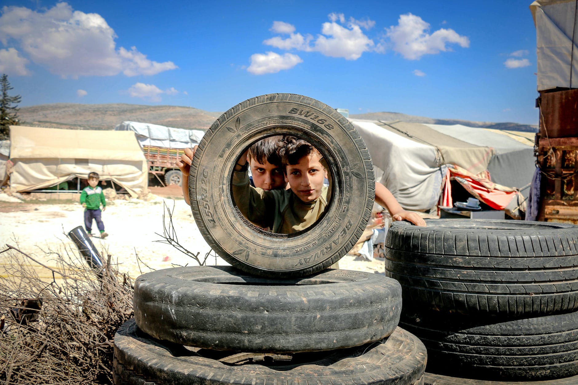 boys looking through car wheel in slum