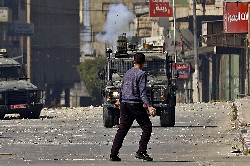 Jovem palestino e comboio militar israelense em Nablus, na Palestina - Zain Jaafar / AFP