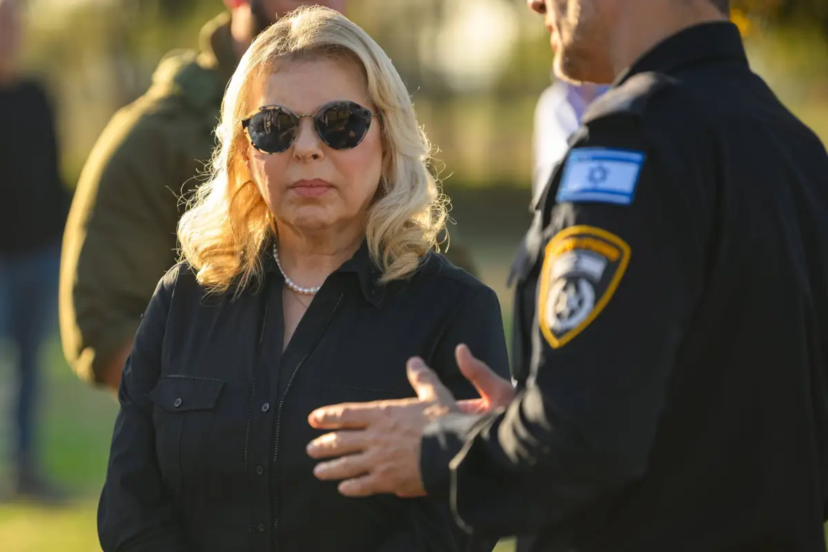 Sara Netanyahu conversa com um membro da polícia israelense enquanto visita um memorial com fotos de pessoas mortas durante o ataque do Hamas ao festival Super Nova, em 30 de novembro de 2023, em Re'im, Israel [Alexi J. Rosenfeld/Getty Images]