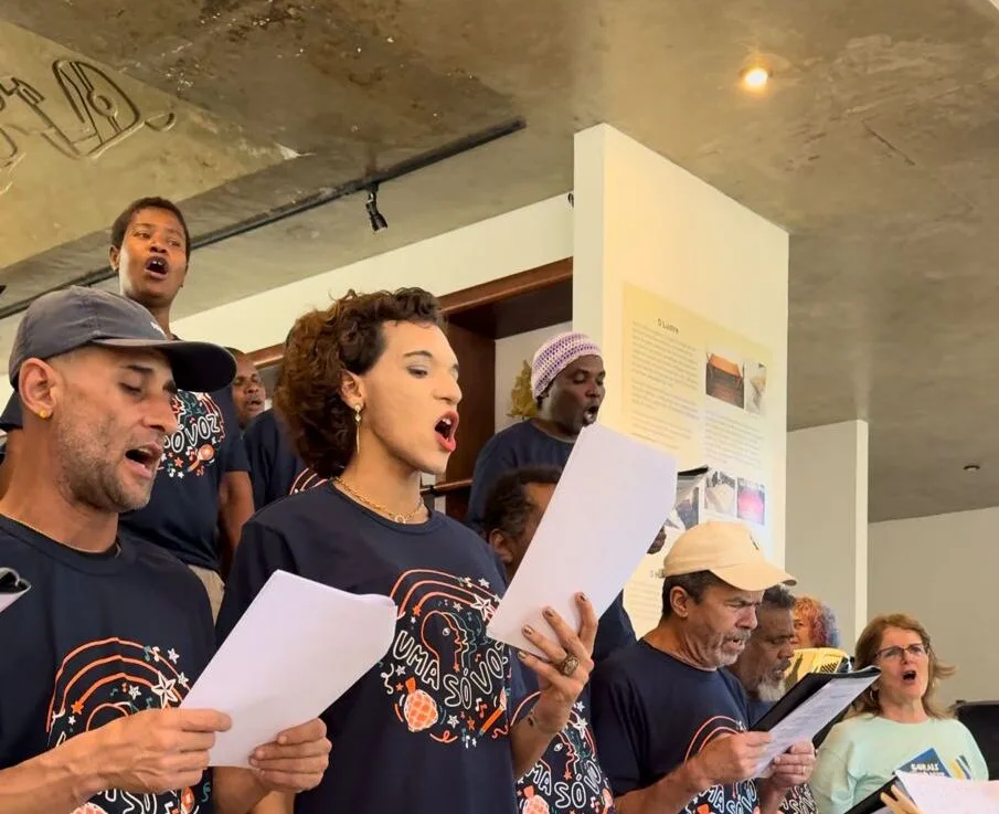 Rio de Janeiro, 14 de agosto – O visitante que chega ao Museu do Amanhã, às quintas-feiras, é instigado a prestar atenção na música que preenche o espaço. O som potente parte de 45 vozes reunidas no canto coral Uma Só Voz, iniciativa do programa Vozes do Amanhã, desenvolvida pelo museu e apresentada pela Volvo. Todas essas vozes têm algo em comum: vêm da garganta de pessoas em situação de rua. “O Uma Só Voz é o ponto de partida das relações que as pessoas vão estabelecer por aqui”, ressalta Fabio Moraes, mediador social do Museu do Amanhã. “Um museu não pode ser pensado só para um público específico, e sim para todos os públicos. Termos o Transportar e o Uma só Voz é uma provocação para todos nós e, assim, exercemos de fato o que o museu se propõe, que é discutir sustentabilidade e convivência.”, ressalta Moraes. Criado em 2016, o Uma Só Voz, cujo repertório é selecionado conjuntamente pelos integrantes e pelo regente Ricardo Branco, reúne-se no Museu do Amanhã semanalmente e se apresenta eventualmente em outros museus e espaços públicos, como consulados, assembleias e câmaras legislativas, além de instituições culturais. Em 2023, o coral fez 79 apresentações e segue a todo vapor em 2024. Transportar Outro projeto dentro do programa Vozes do Amanhã é o Transportar, desenvolvido com pessoas LGBTQIA+ abrigadas nos CPA (Centro Provisório de Acolhimento) da prefeitura. Qualquer pessoa, porém, pode fazer parte da iniciativa, desde que haja vaga. O grupo se reúne às sextas-feiras e conta com cerca de 35 pessoas, todas vivendo em vulnerabilidade social, muitas delas na rua. O carro-chefe do projeto é o teatro e a produção de espetáculos. Contando com a parceria do coletivo Transparente, que também trabalha com a temática LGBTQIA+, o Transportar está em seu 4º ano de existência, se apresentando em diversos espaços e usa o teatro para discutir temas relevantes para a população LGBTQIA+. Muito além da arte Tanto o Uma Só Voz como o Transportar atuam em cinco eixos temáticos. O primeiro é o eixo de Arte e Cultura, materializado através do coral e do grupo teatral; o segundo é o da Saúde física e Mental, desenvolvido por meio do trabalho semanal de uma psicóloga que apoia a equipe e trabalha com escutas terapêuticas e arteterapia, além da parceria com projetos como o Consultório de Rua, da prefeitura do Rio. O terceiro eixo é o da Empregabilidade, auxiliando, dialogando e buscando parcerias que possam oferecer oportunidades aos inscritos; o quarto é o da Educação, incentivando a retomada dos estudos por parte dos inscritos – o projeto celebra o êxito de que 30% dos participantes voltaram a estudar. Por último, o eixo de Direitos Humanos e Incidências Políticas, que propõe discussões sobre direitos e deveres e reflexões sobre a vida na rua, além de ajudar o acesso a direitos básicos, como a obtenção de documentos e auxílios governamentais.