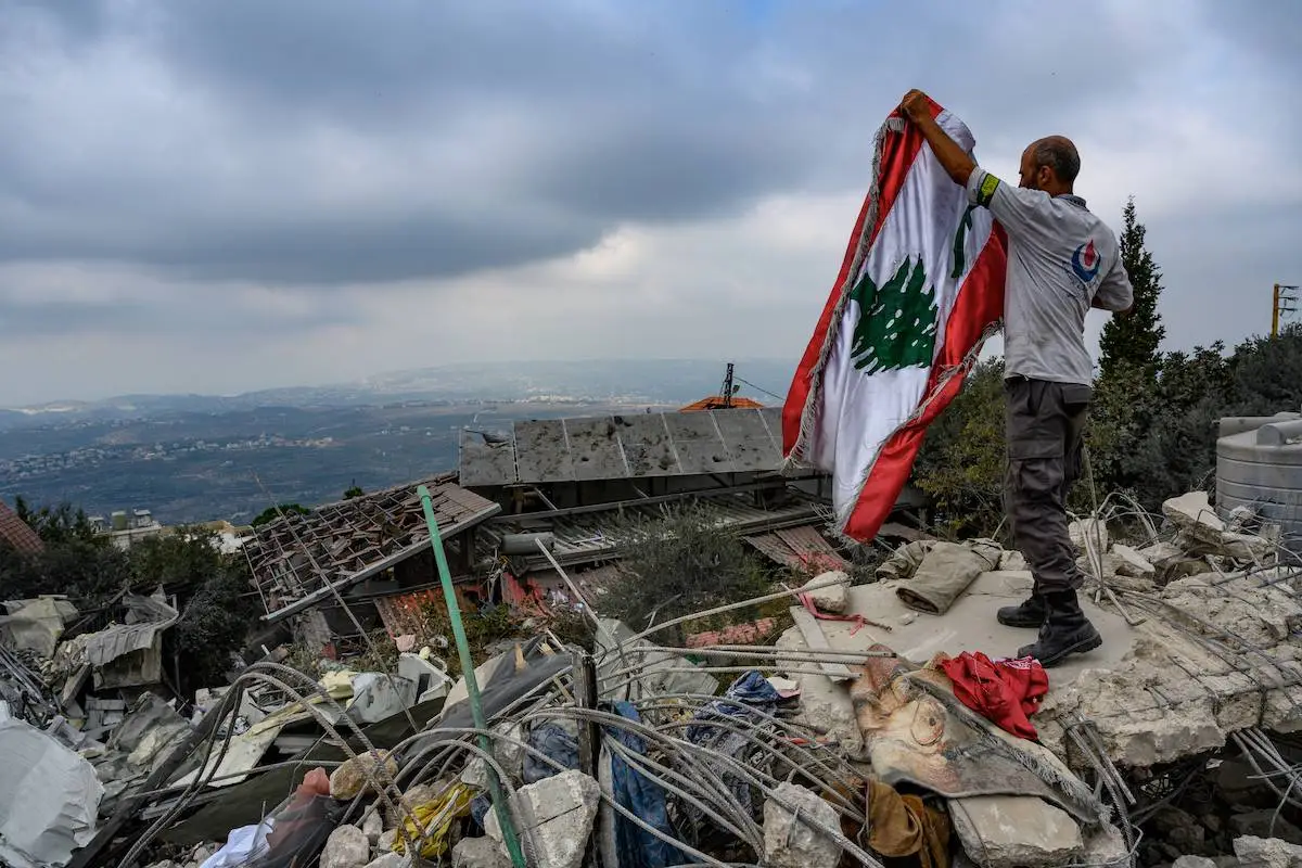 Membro da defesa civil ergue bandeira libanesa entre os escombros deixados por ataques de Israel a Deir Billa, no Líbano, em 13 de outubro de 2024 [Scott Peterson/Getty Images]