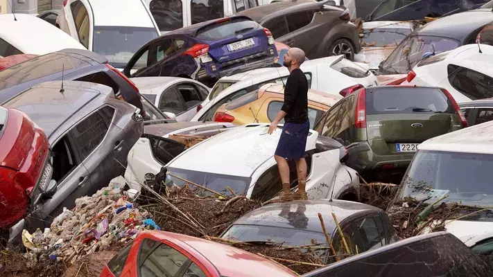 Homem anda sobre pilha de carros após temporal atingir Valência, na Espanha. Foto: reprodução