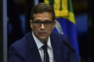 São Paulo – O prefeito Ricardo Nunes (MDB) convidou o presidente do Banco Central, Roberto Campos Neto, para integrar sua equipe de governo. O convite foi feito nesta segunda-feira (23), mas Campos Neto declarou que pretende tirar dois meses de descanso após deixar o cargo, em janeiro. Paralelamente, o governador de São Paulo, Tarcísio de Freitas (Republicanos), também demonstrou interesse em contar com o economista em sua gestão. Analistas veem a possível parceria como um movimento estratégico para as eleições de 2026. Campos Neto e o futuro político da direita Campos Neto se destaca como peça central nos planos políticos da centro-direita. Ele é cotado para fortalecer uma eventual candidatura presidencial de Tarcísio de Freitas, que, segundo interlocutores, só renunciaria ao governo paulista em 2026 com aval do ex-presidente Jair Bolsonaro (PL). Bolsonaro, porém, enfrenta incertezas devido à sua inelegibilidade. Analistas apontam similaridades com o cenário de 2018, quando Lula (PT) insistiu em sua candidatura até o último momento, apesar dos entraves jurídicos. A articulação da centro-direita Além de Campos Neto e Tarcísio, outros nomes ganham força na direita brasileira, como os governadores Romeu Zema (MG), Ratinho Júnior (PR) e Ronaldo Caiado (GO). Esses líderes buscam se distanciar do extremismo associado a Bolsonaro e reposicionar a direita no espectro político. O PP, partido comandado por Ciro Nogueira, já adota uma postura mais moderada, alinhando-se ao centro, estratégia que sinaliza um movimento para isolar Bolsonaro e abrir espaço para novas lideranças. Perfil técnico e críticas ao Banco Central Campos Neto é reconhecido por seu perfil técnico, mas enfrentou duras críticas do PT e do governo federal durante sua gestão no Banco Central. As reclamações se concentraram na alta dos juros para conter a inflação, ação considerada por alguns como sabotagem à economia. Apesar disso, Campos Neto ainda é visto como um nome de peso. Marqueteiros avaliam que seu perfil técnico e apelo de propostas concretas podem atrair um público cansado de disputas ideológicas. Planos de Campos Neto após deixar o Banco Central Atualmente, Campos Neto trabalha em um livro sobre sua gestão no Banco Central. Durante uma palestra em junho, ele descartou especulações sobre seu futuro imediato: “Já falaram que eu vou abrir fintech, trabalhar na indústria ou ser ministro. A única coisa certa é que vou descansar durante esse tempo”. Entenda o caso: Campos Neto e a disputa por sua liderança Convites: Ricardo Nunes e Tarcísio de Freitas disputam Campos Neto para suas gestões. Eleições 2026: Campos Neto pode fortalecer uma candidatura de Tarcísio. Perfil técnico: Reconhecido no mercado financeiro, ele enfrenta críticas da esquerda. Cenário político: Centro-direita busca novos nomes para se distanciar de Bolsonaro. Descanso: Campos Neto afirmou que priorizará um período de descanso após janeiro.