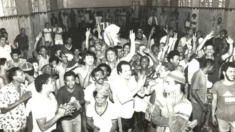 A imagem histórica, feita pelo célebre fotojornalista Alcyr Cavalcanti (1936-2024), mostra uma festa dentro do Presídio da Ilha Grande, promovida pelos membros da Falange Vermelha, que logo se tornaria o Comando Vermelho, para comemorar a morte de diversos membros da facção rival, a Falange Jacaré, em 1979. Foto: Alcyr Cavalcanti, CC BY