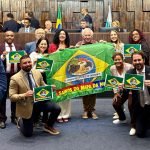 Deputados de oposição exibem bandeira na Alerj para celebrar a saída do Brasil do mapa da fome. Parlamentares bolsonaristas reagem com ironias durante sessão.