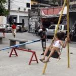 Crianças brincam em praça da Vila Cruzeiro ao lado de barricadas que foram colocadas para conter avanço de policiais durante a Operação Contenção. Foto: Tânia Rêgo/Agência Brasil