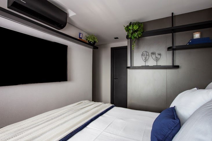 ✨ Parede em Frente à Cama: 5 Ideias Criativas para um Quarto Protagonista | Diário Carioca Trabalhando o cinza como a cor base deste dormitório, a arquiteta Mari Milani trouxe apenas a prateleira e o ar-condicionado (ambos no preto) para ocupar o espaço da parede, deixando a TV como a protagonista no setor, posicionada bem ao centro | Foto: Mariana Camargo