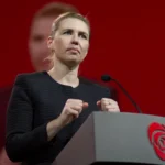 Foto de Mette Frederiksen em pronunciamento oficial, com fundo institucional. O texto aborda reforço militar da Dinamarca e OTAN no Ártico, em resposta à pressão dos EUA sobre a Groenlândia.